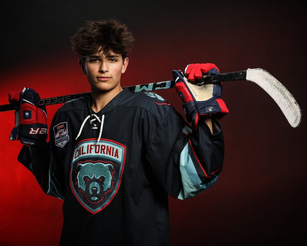 Hockey player in California bear jersey holding stick over shoulder against red backdrop