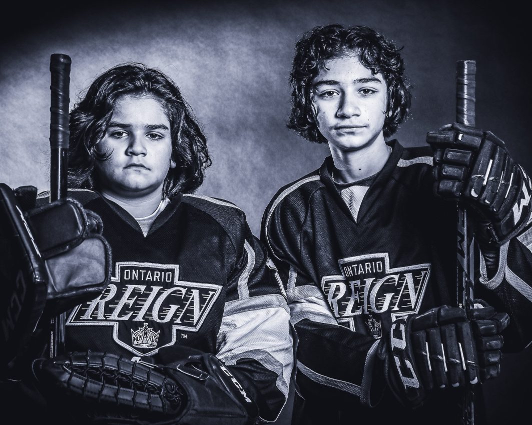 Two youth hockey players in Ontario Reign jerseys with sticks in black and white