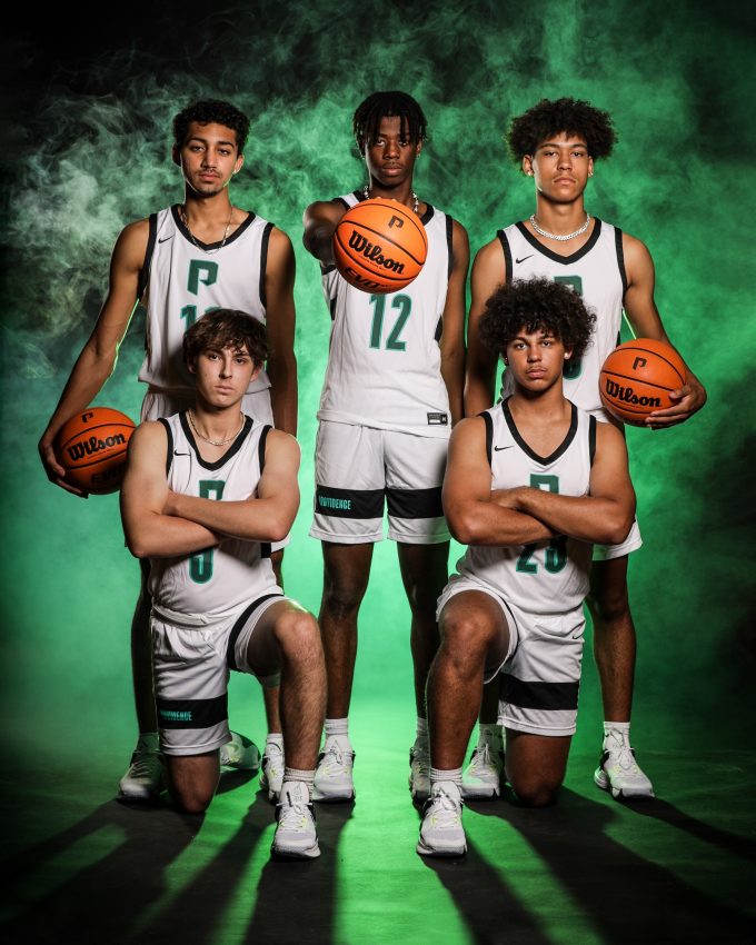 Five basketball players in white uniforms with Wilson basketballs and green smoke backdrop
