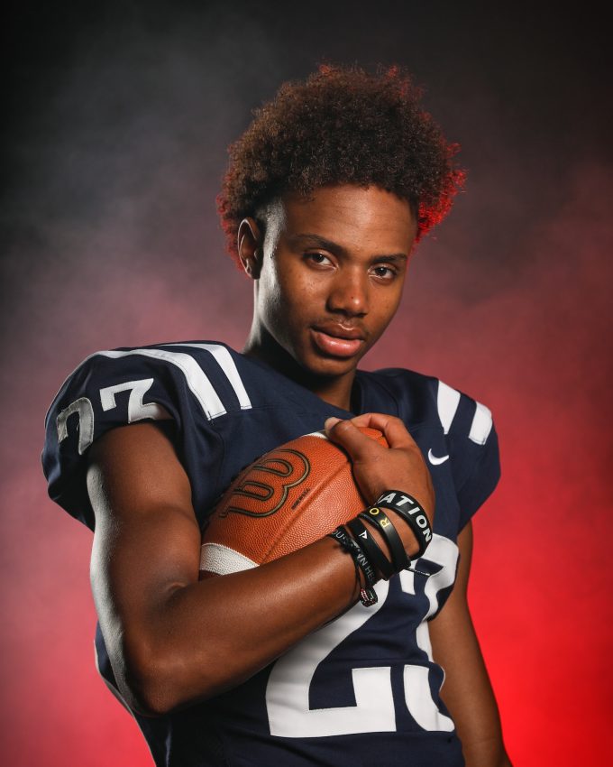 Football player in navy jersey holding football with dramatic lighting